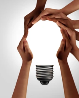 multiple people's hands shaped together to frame a lit lightbulb